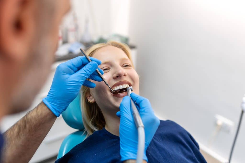 Dentist smiling and communicating with a young woman while checking her teeth during a dental fillings procedure in Dorchester.